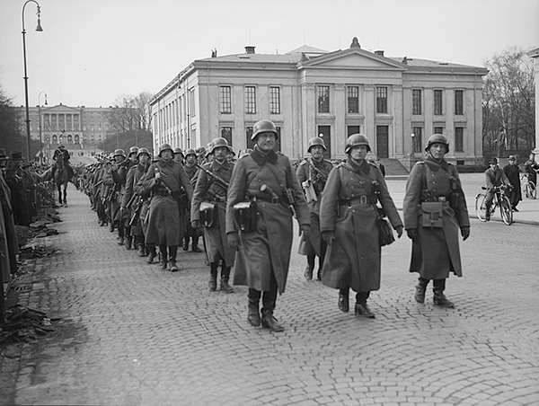 Bildet viser soldater som marsjerer med en stor hvit bygning i bakgrunnen
