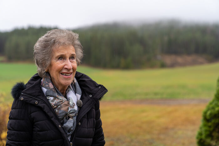 Eldre kvinne, vinterkledd, åkerlandskap i bakgrunnen
