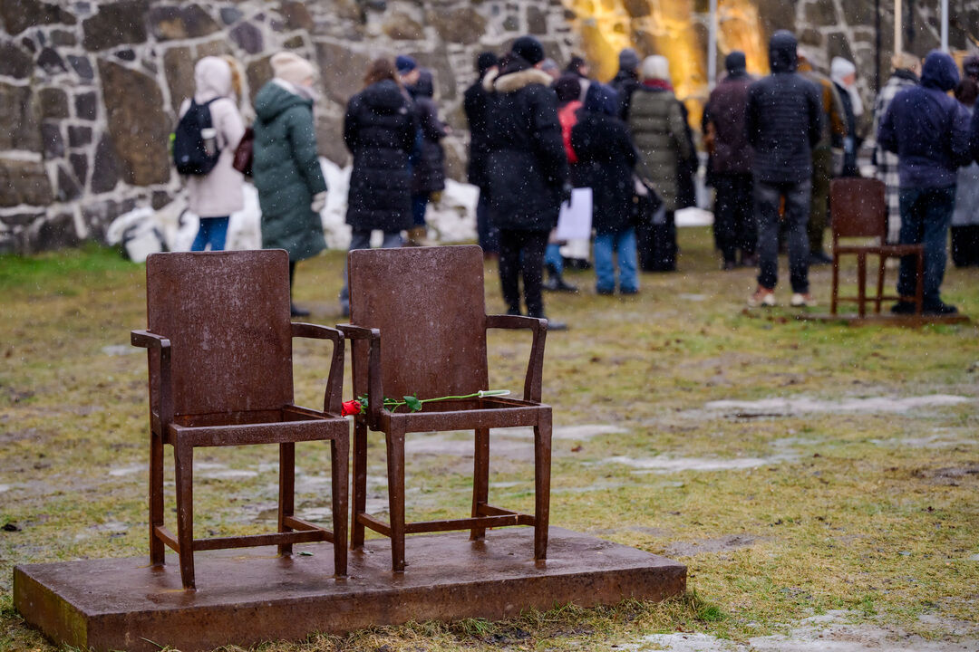 To tomme stoler med en rød rose. Folkemengde i bakgrunnen.