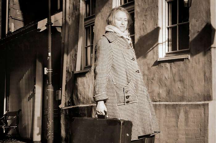 Bildet viser en ung kvinne med rutete kåpe og en koffert i hånden