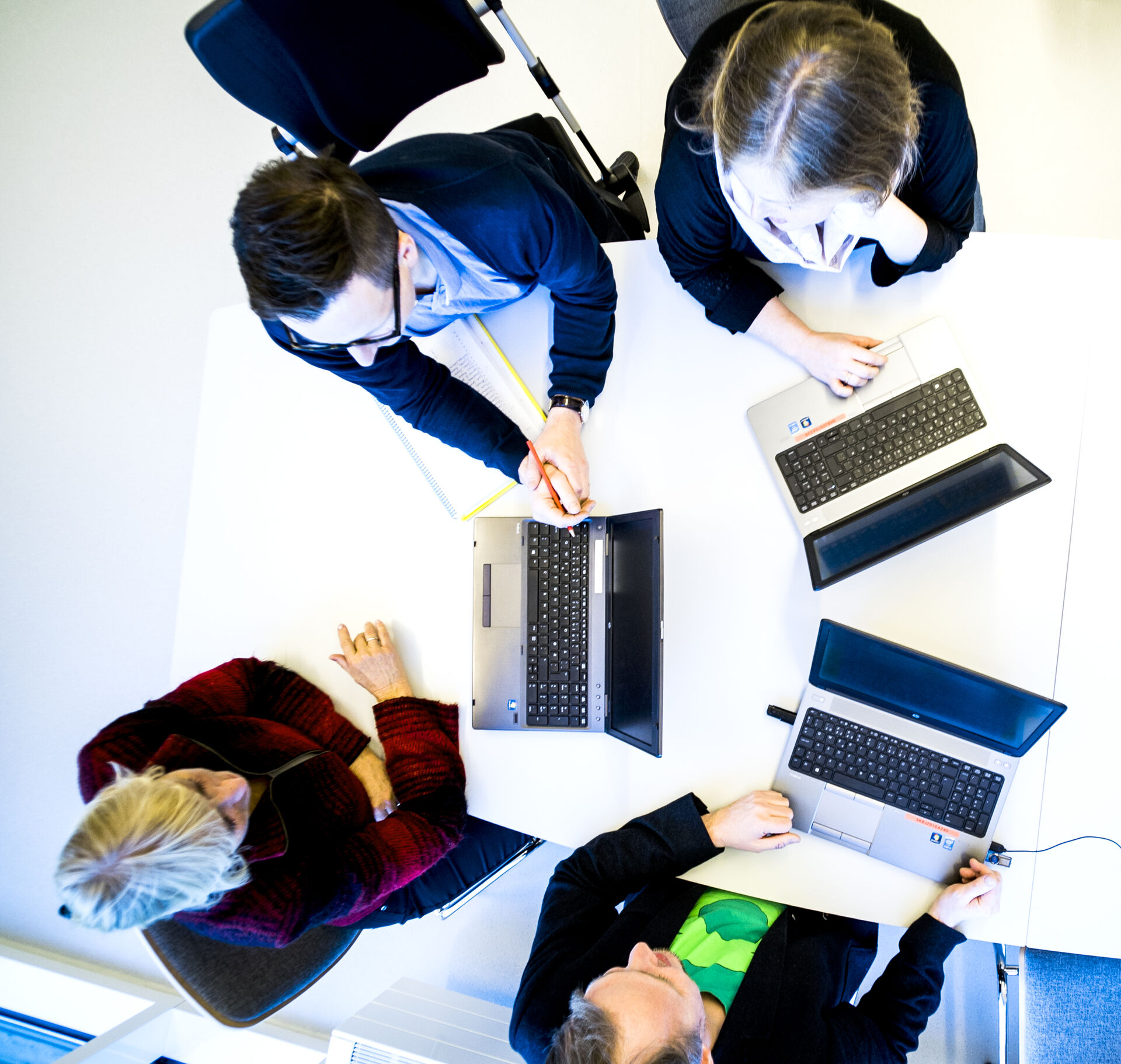 Fire personer som sitter med hver sin laptop rundt et bord