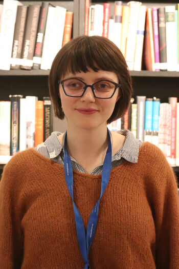 Karianne Hansen, forsker og historiker. Står foran bohylle og ser rett i kamera.