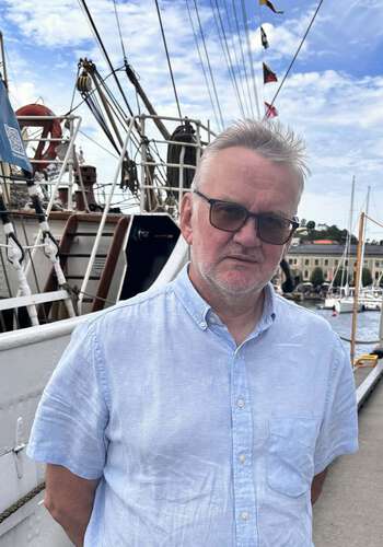portrettfoto av en voksen mann foran en seilskute