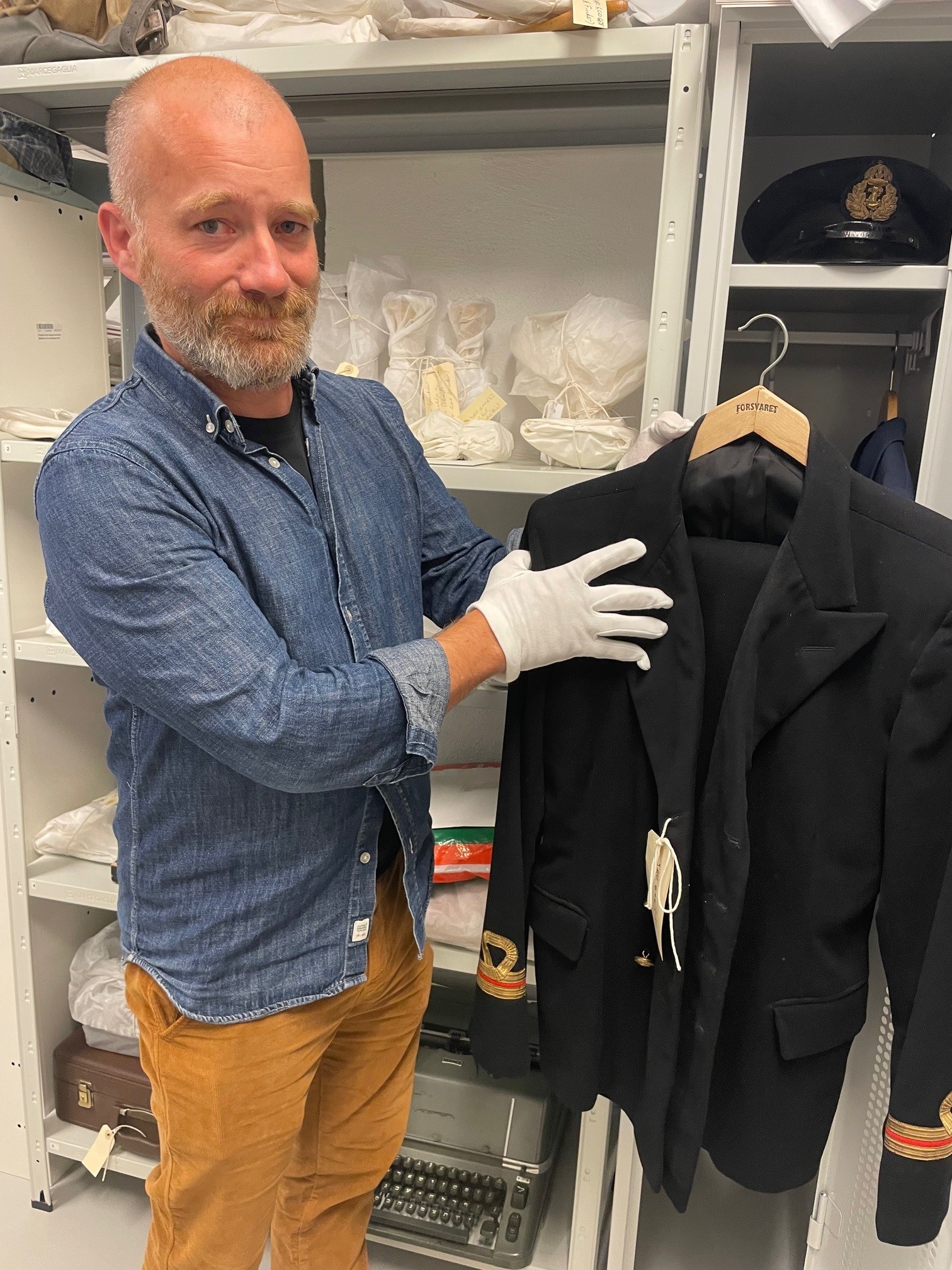 Faglig leder Mats Tangestuen ved Jødisk Museum i Oslo viser fram Bernhard Goldbergs uniform. På hyllen bak ligger hans uniformslue. Foto: Hilde Harbo