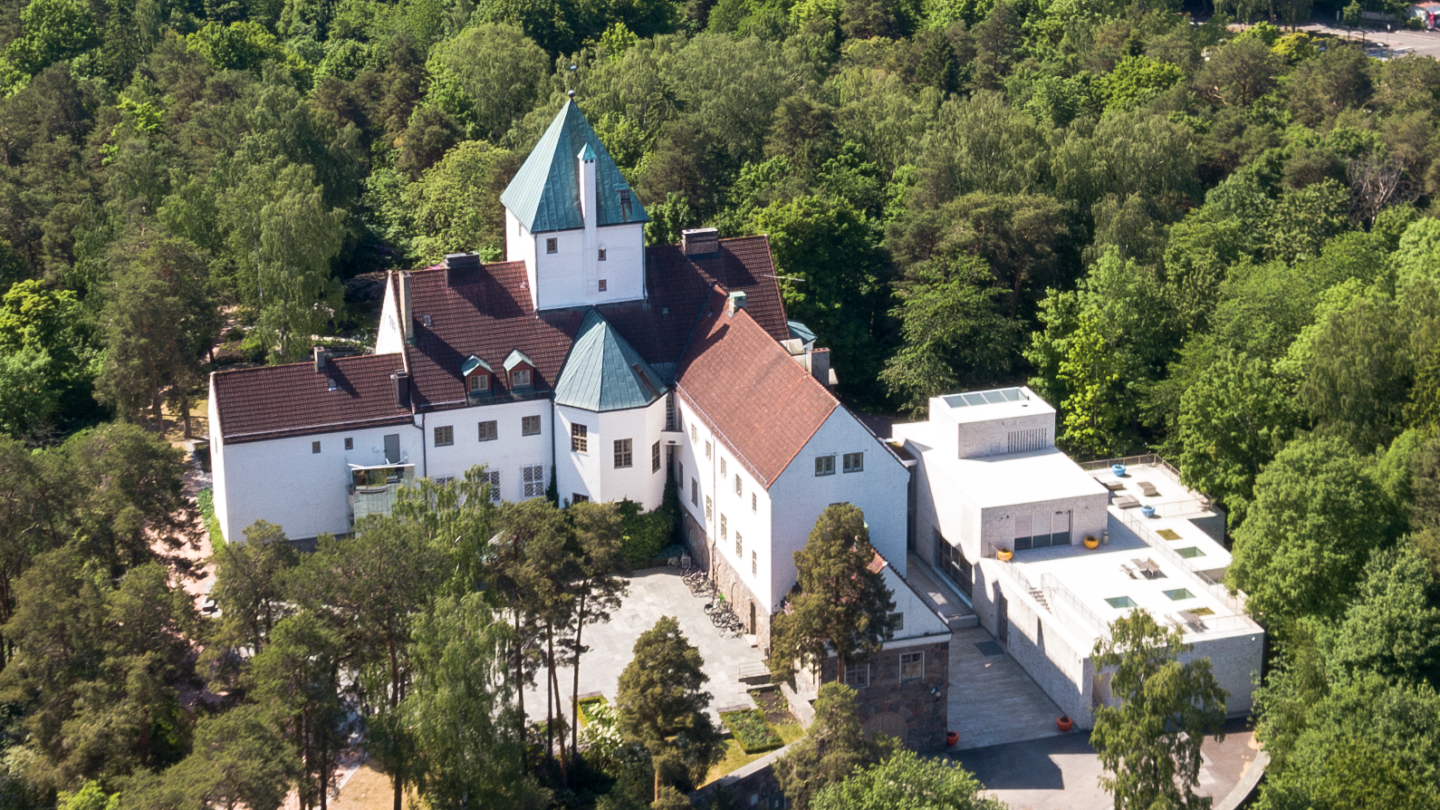 Grand, white building with a tower. Woods all around.