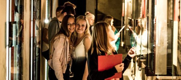 Smilende ungdommer i et rom med montere med bilder og tekst
