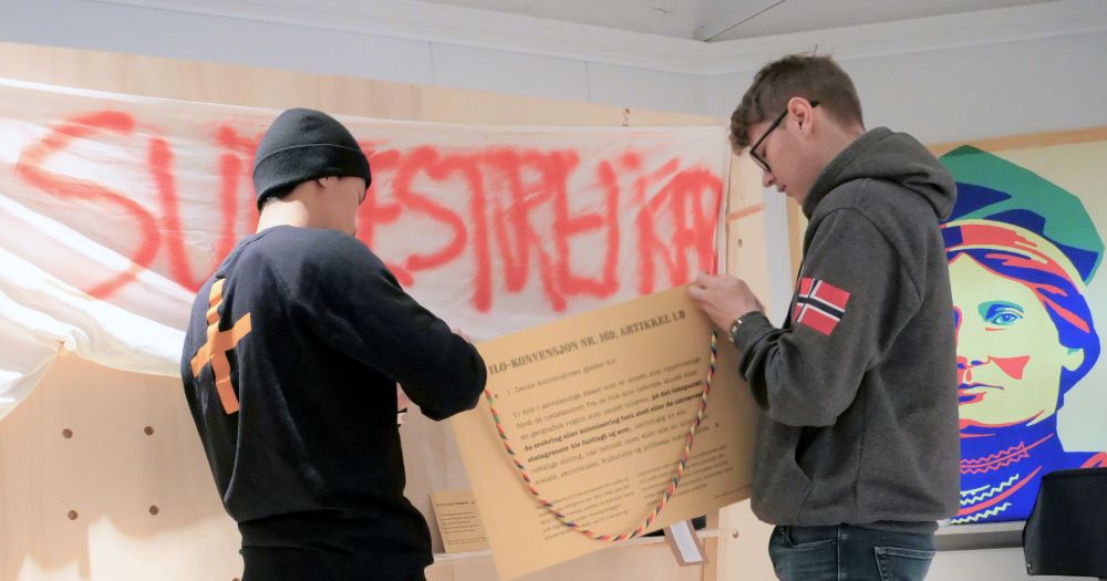 To unge gutter henger opp en plakat 